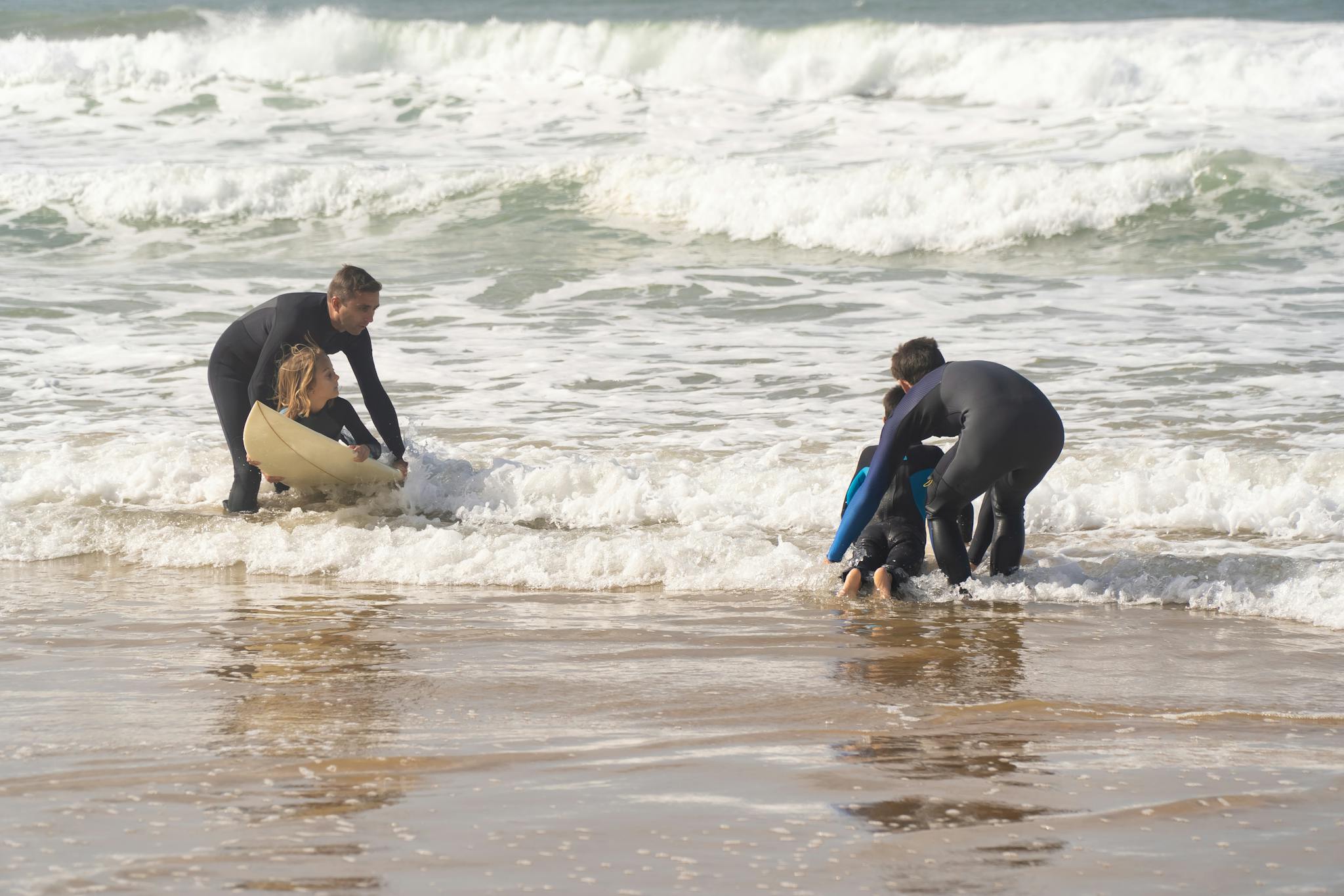 Children learning to surf on a sunny day at a Portuguese beach with instructors.